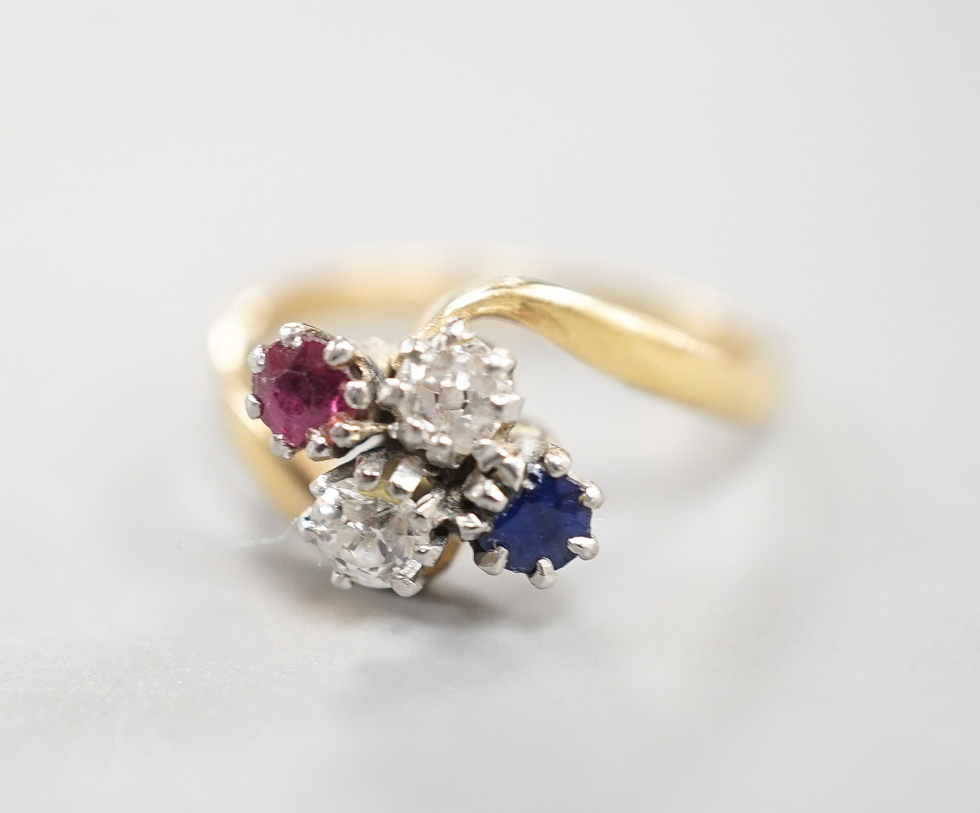 An early 20th century 18ct & plat, ruby, sapphire and diamond set four stone crossover ring, size M, gross weight 4 grams.